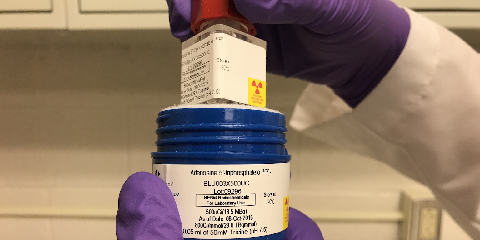 Gloved hands holding a jar of radioactive materials.