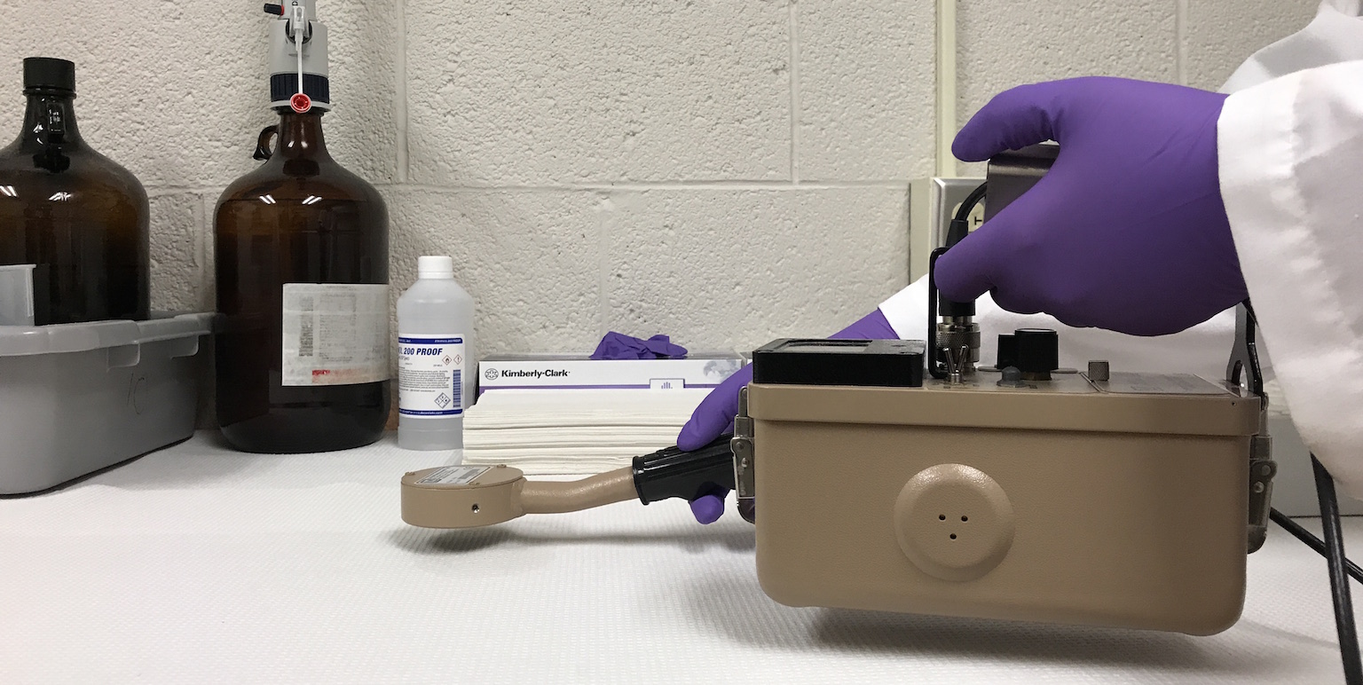 Gloved hands holding a machine that detects radiation.